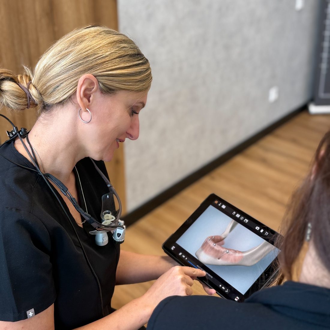 Zahnärztin Adela Deac erklärt einer Patientin am Tablet, wie feste Zähne auf Implantaten sitzen