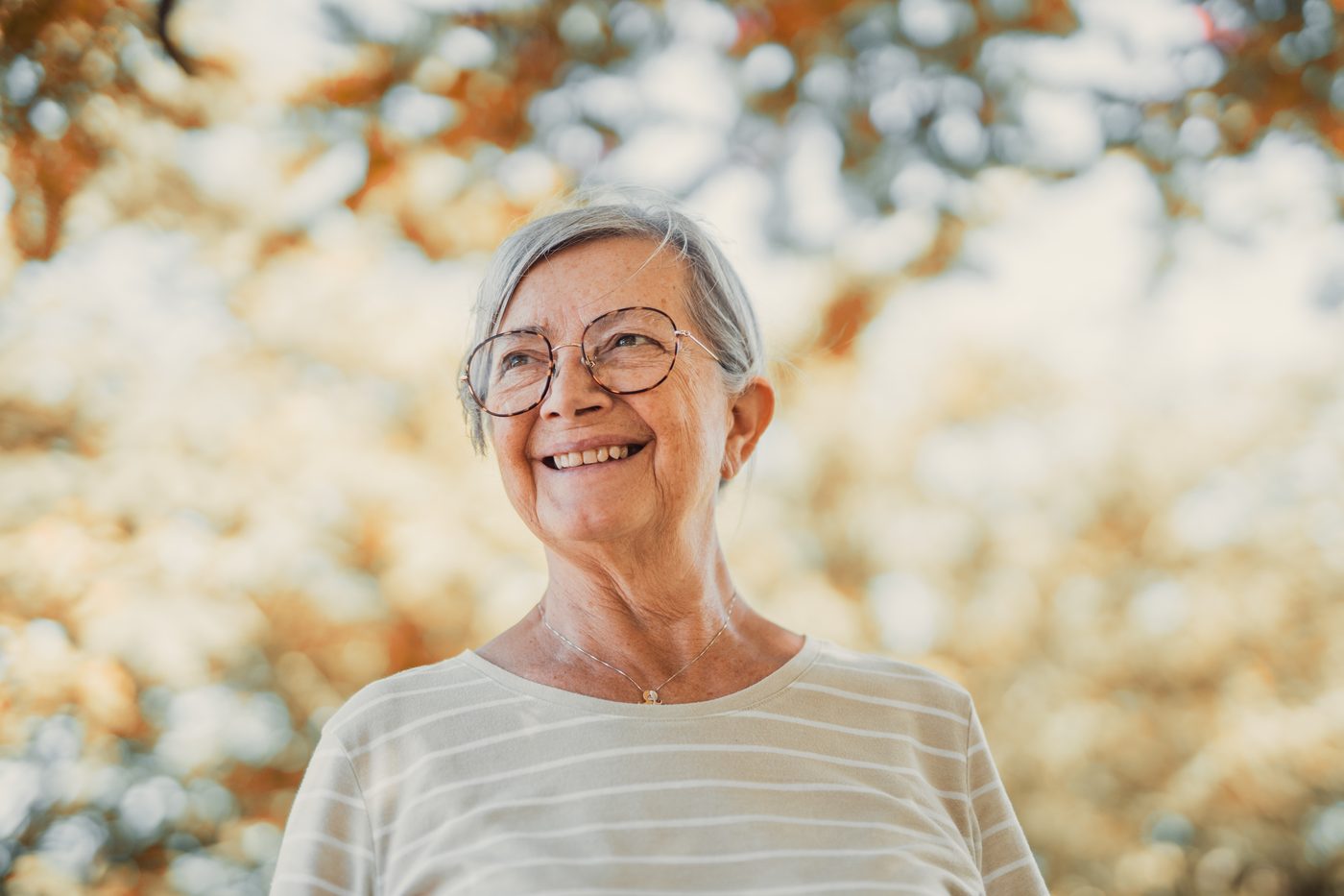 Lächelnde ältere Frau mit Brille unter Herbstlaub